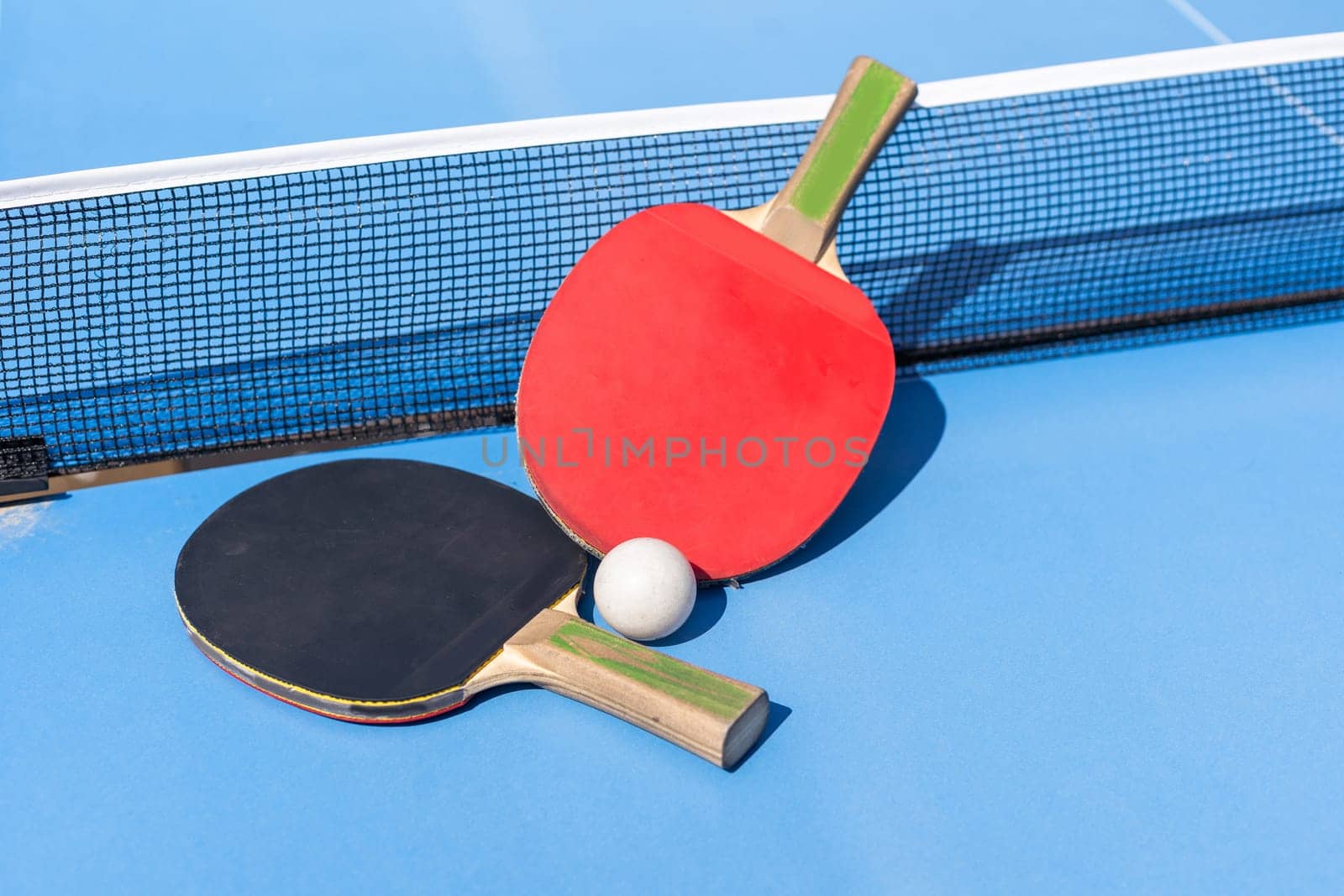 Two table tennis or ping pong rackets and ball on blue table with net by Andelov13