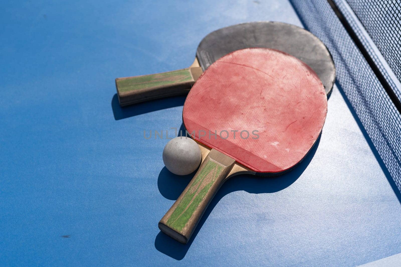 Two table tennis or ping pong rackets and ball on blue table with net by Andelov13