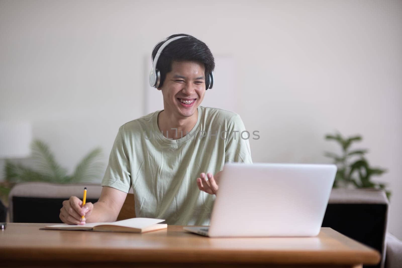 Young Asian student doing homework and studying online, online video call on laptop happily at home by wichayada