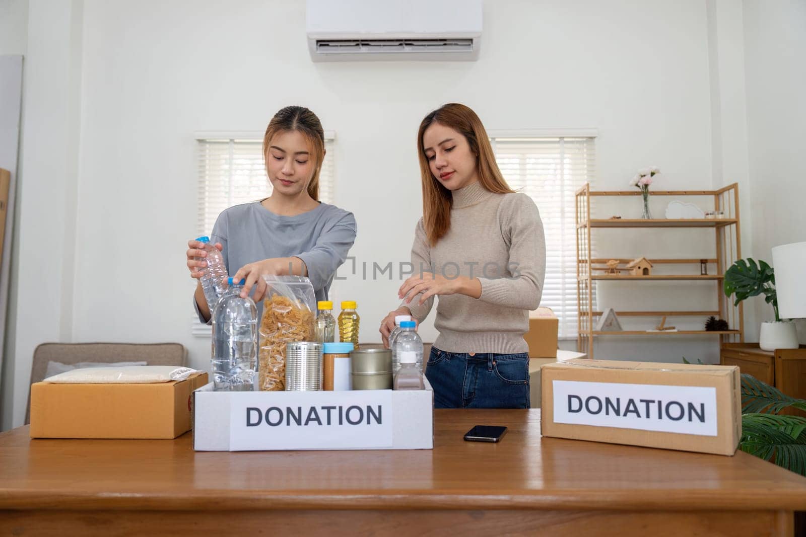 Happy young woman volunteer collecting, sorting food for needy people, team working together on donation project in charitable at home by nateemee