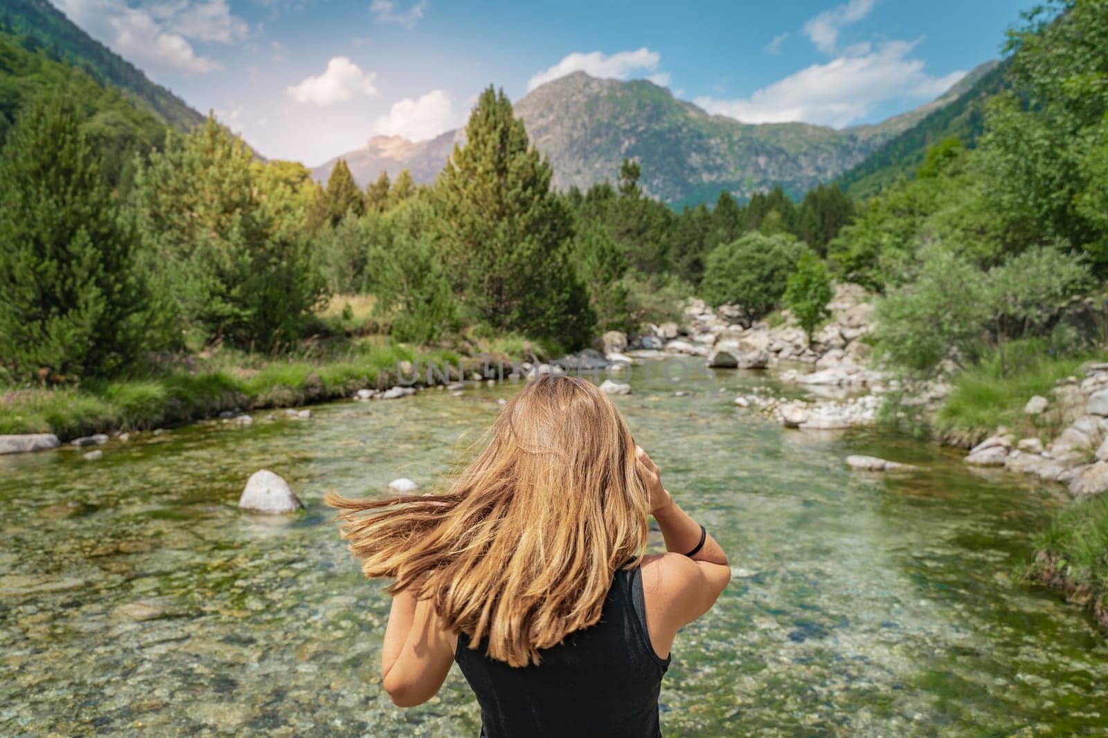 Summer background with a girl with golden blonde hair in front of a crystal clear river and high mountain. High quality photo