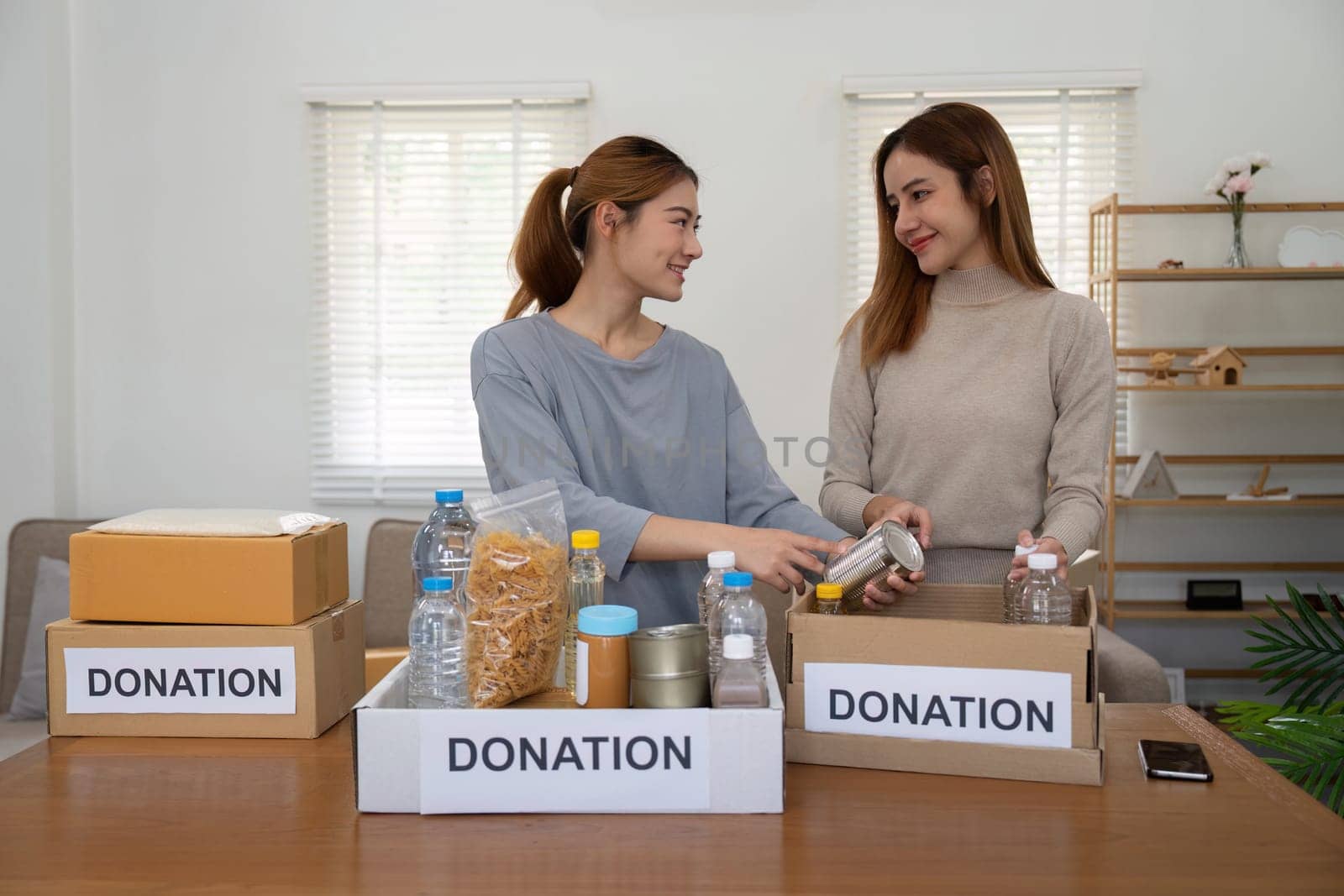 Happy young woman volunteer collecting, sorting food for needy people, team working together on donation project in charitable at home by nateemee
