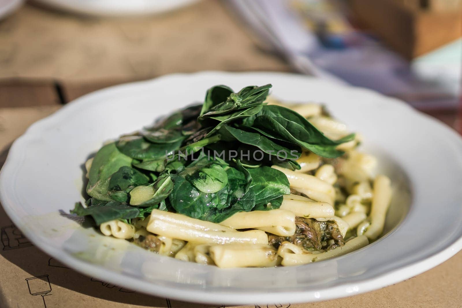Spring pasta penne with basil pesto and sweet pea in a bowl on a rustic wooden background in street cafe by Satura86