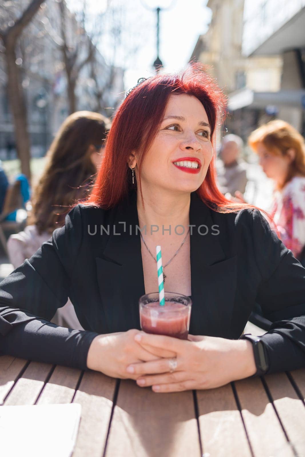 Beautiful happy woman with long red hair enjoying cocktail in a street cafe by Satura86