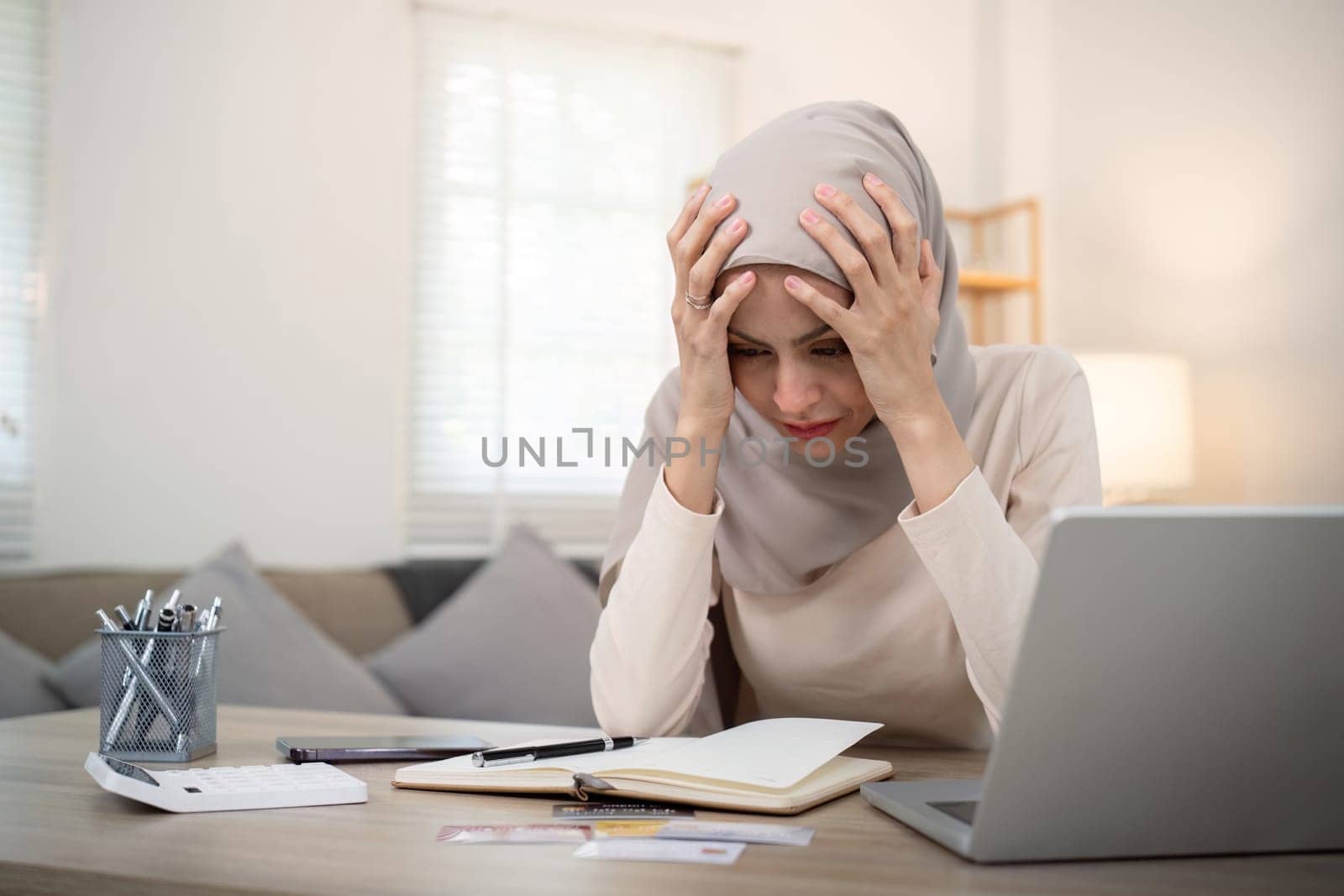 Muslim woman calculate using calculator and invoice bill document with stress young muslim woman covering head she is having financial problem.