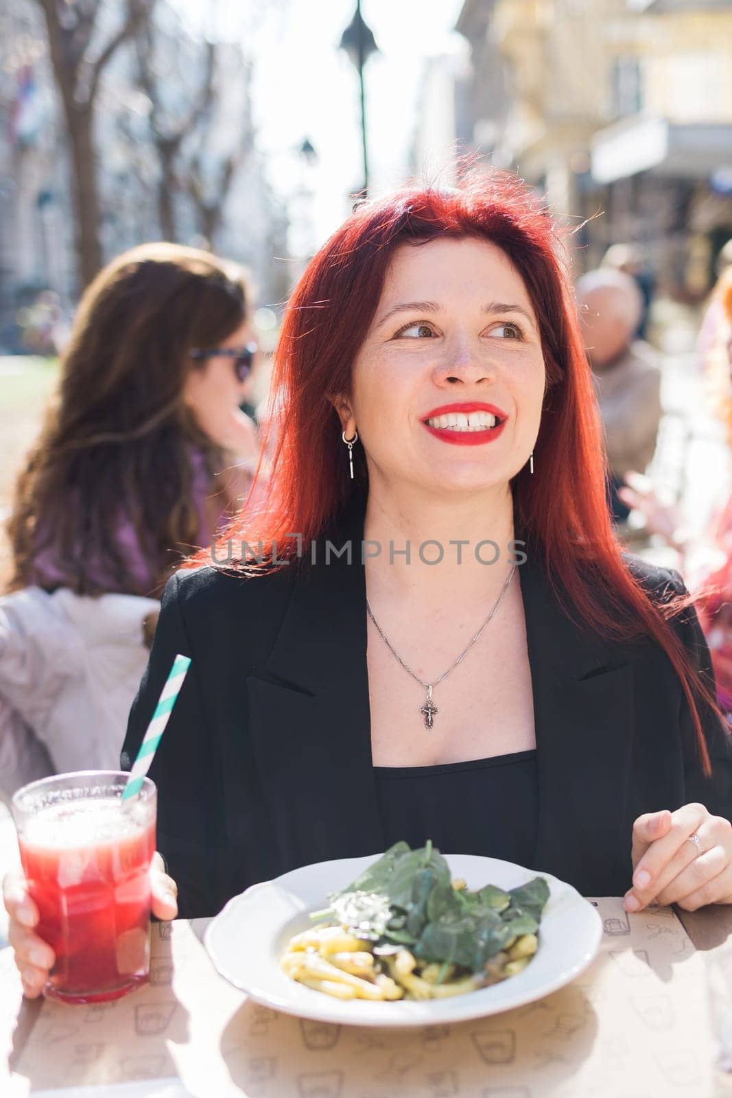 Millennial woman eating italian pasta at restaurant on the street in spring. Concept of Italian gastronomy and travel. Stylish woman with red hair.