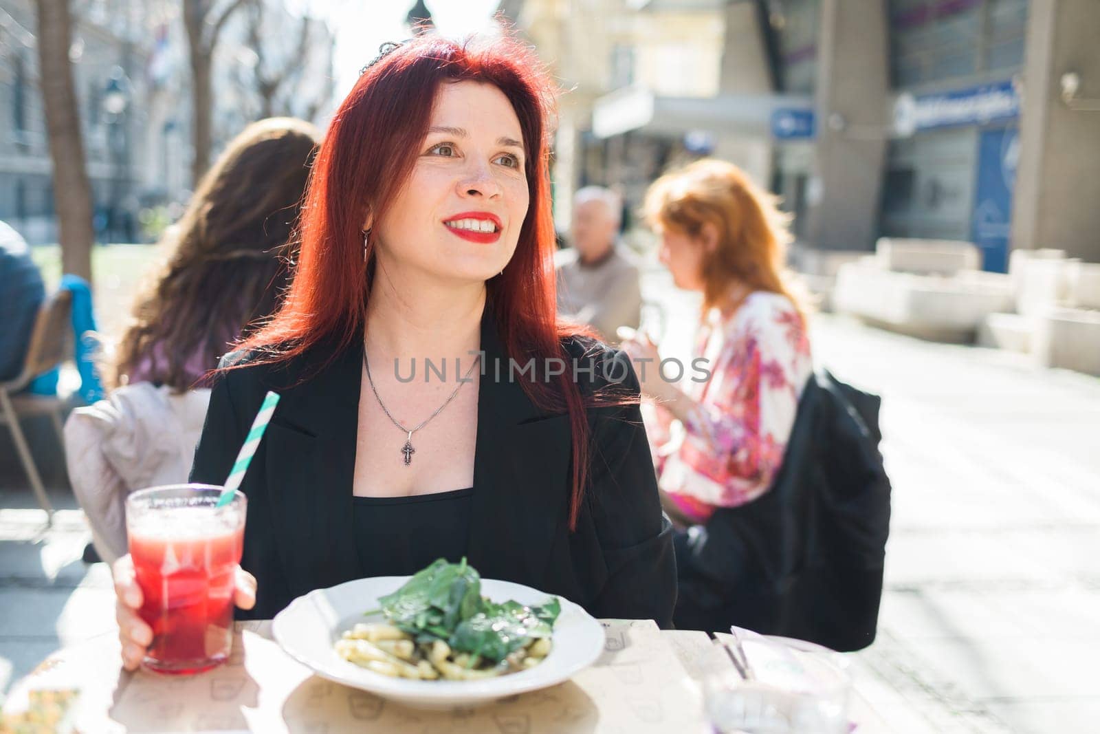 Beautiful happy woman with long red hair enjoying pasta in a street cafe