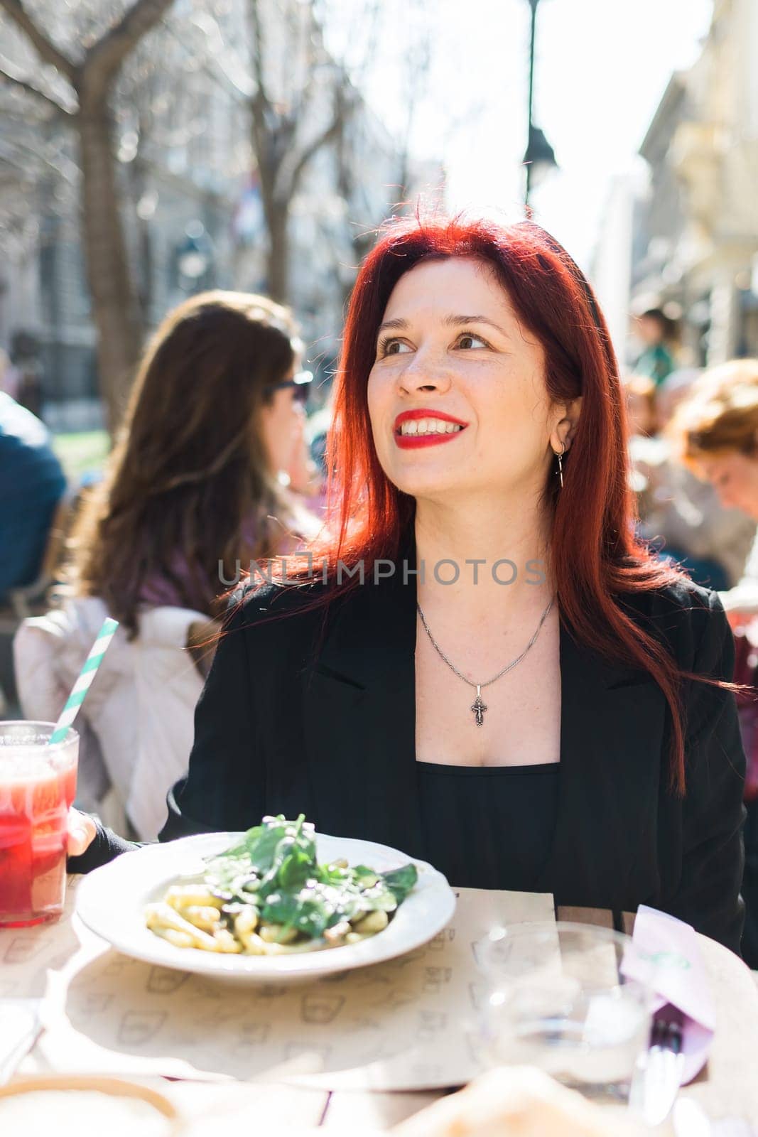 Millennial woman eating italian pasta at restaurant on the street in spring. Concept of Italian gastronomy and travel. Stylish woman with red hair by Satura86