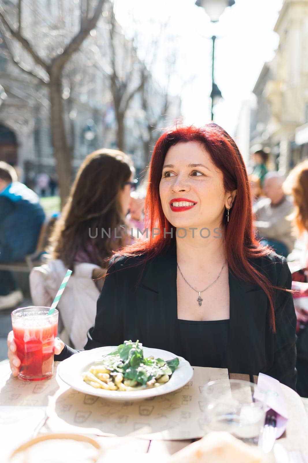 Beautiful happy woman with long red hair enjoying pasta in a street cafe