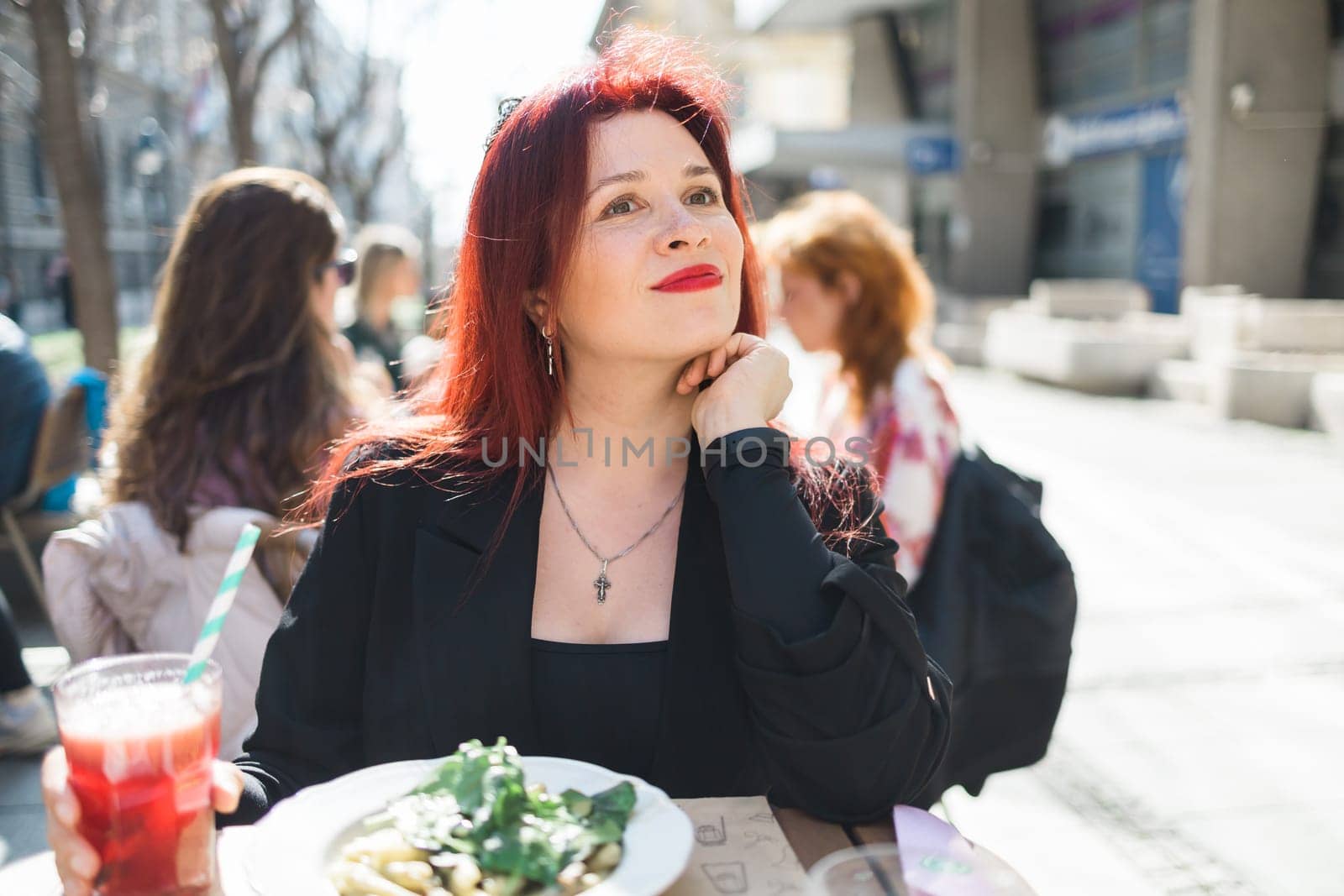 Beautiful happy woman with long red hair enjoying pasta in a street cafe