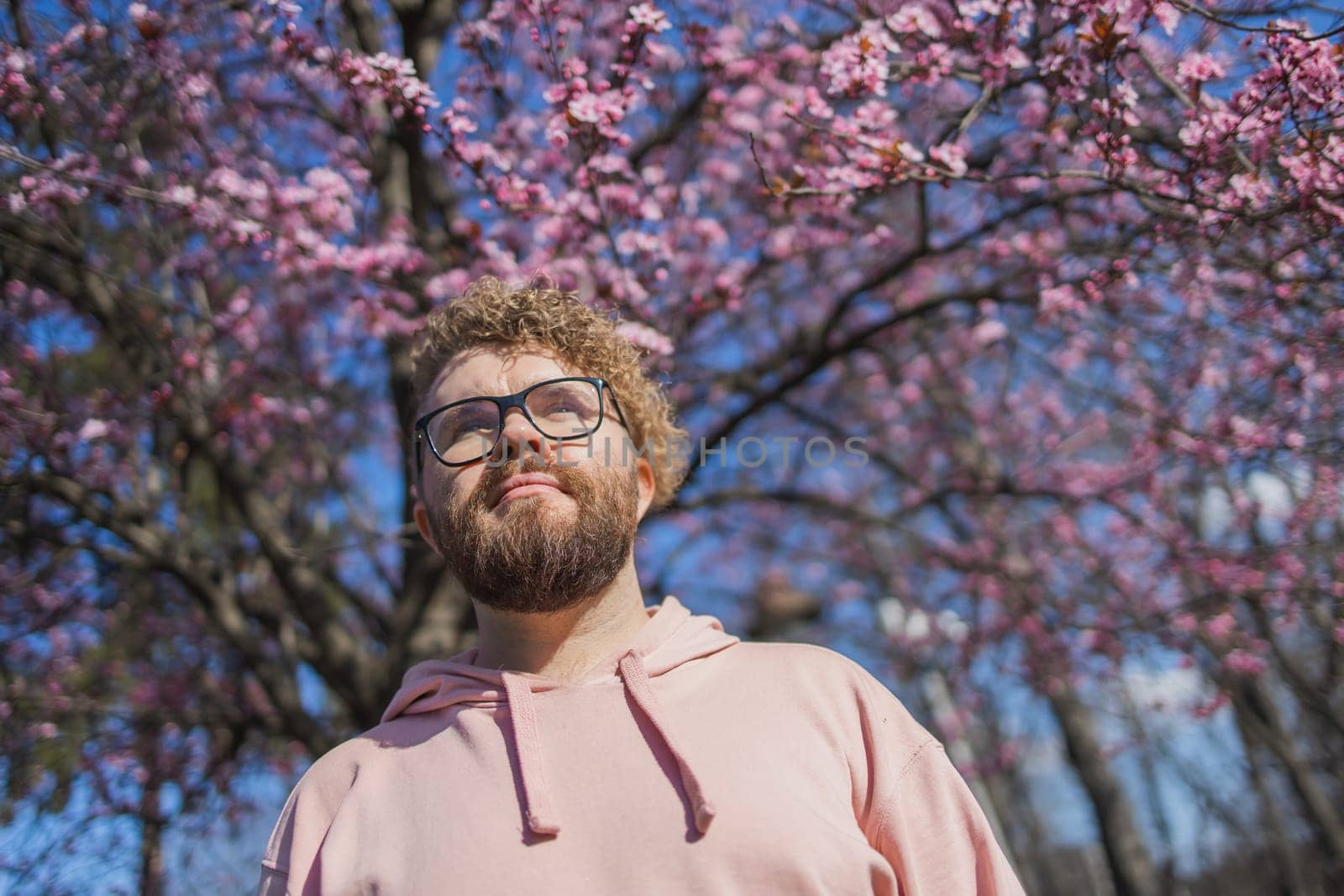 Man allergic enjoying after treatment from seasonal allergy at spring. Portrait of happy bearded man smiling in front of blossom tree at springtime. Spring blooming and allergy concept. Copy space.