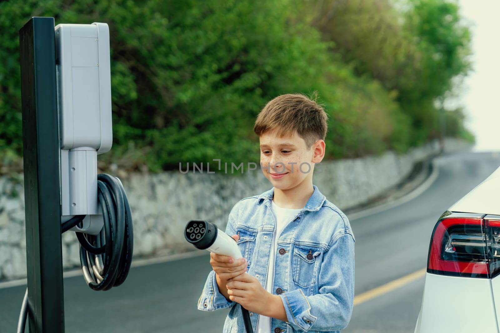 Little boy recharging electric car from EV charging station. Perpetual by biancoblue