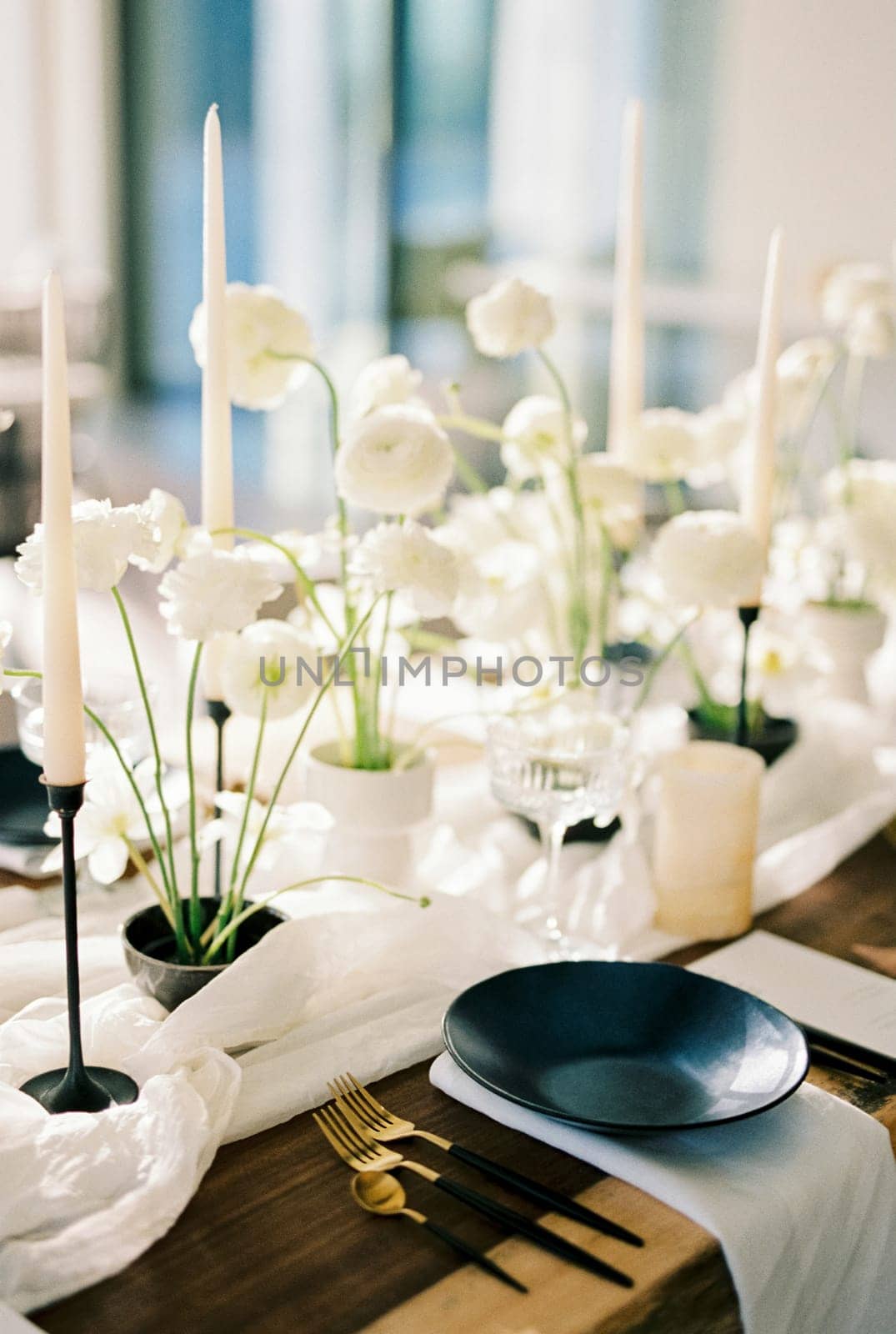 Black plates stand on a wooden table next to white bouquets of flowers on a narrow tablecloth. High quality photo