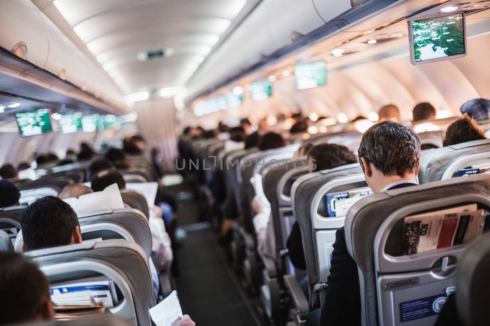 Interior of airplane with passengers on seats and stewardess in uniform walking the aisle, serving people. Commercial economy flight service concept