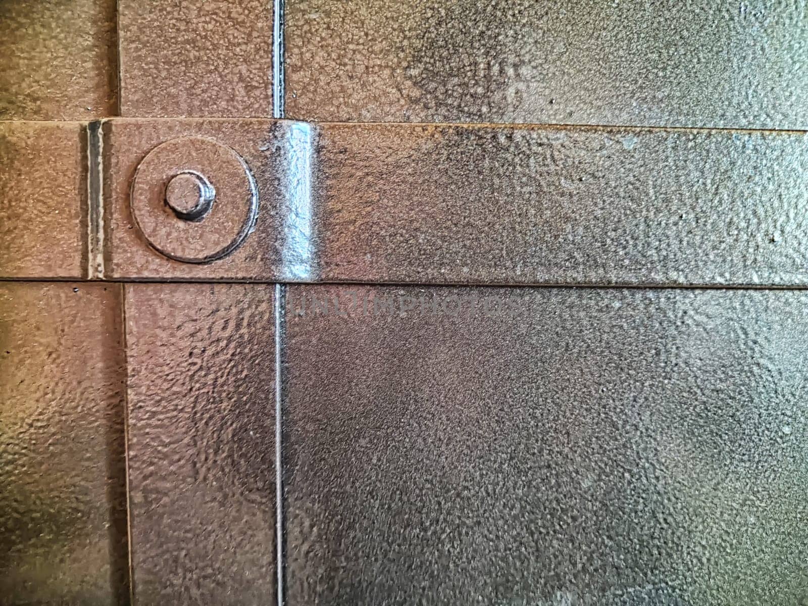 Forged rivet on a metal door or wall. Background, texture. Forged steel rivet connecting textured metal plates