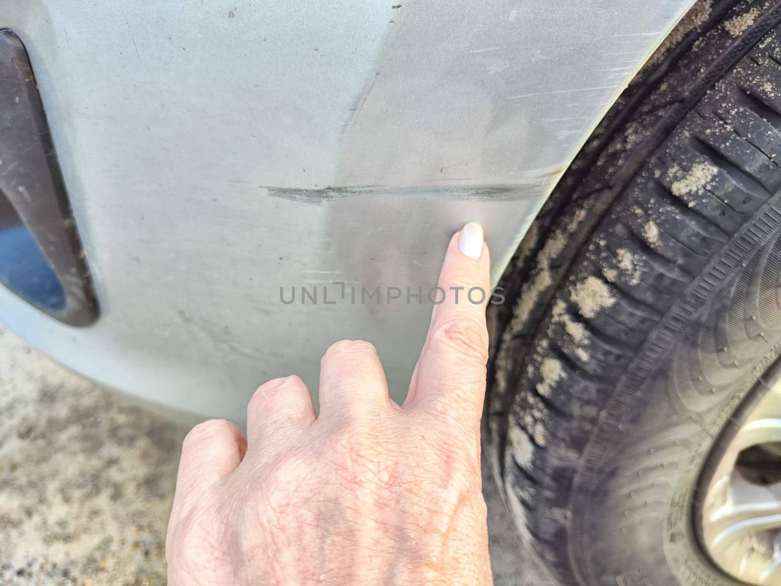 Finger indicating a scratch on a vehicles fender. Close-Up of Scratched Car Fender With Finger Pointing