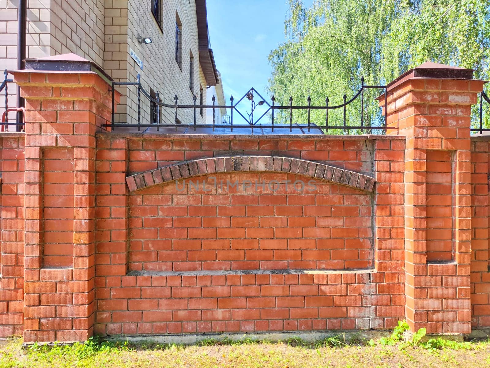 Red Brick Wall With Arch Detail in Urban Setting. Red brick wall featuring an arch design on sunny day