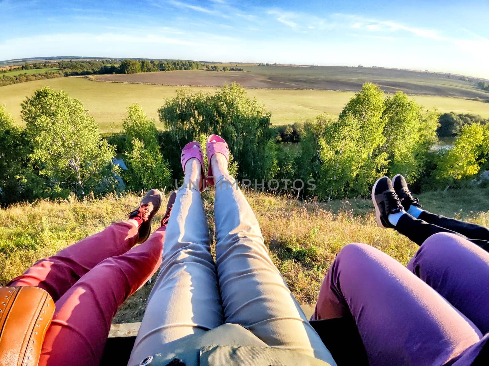 Legs of people on a swing over a beautiful natural landscape in summer or spring. Friends Enjoying Scenic Overlook at Sunset the view from hilltop