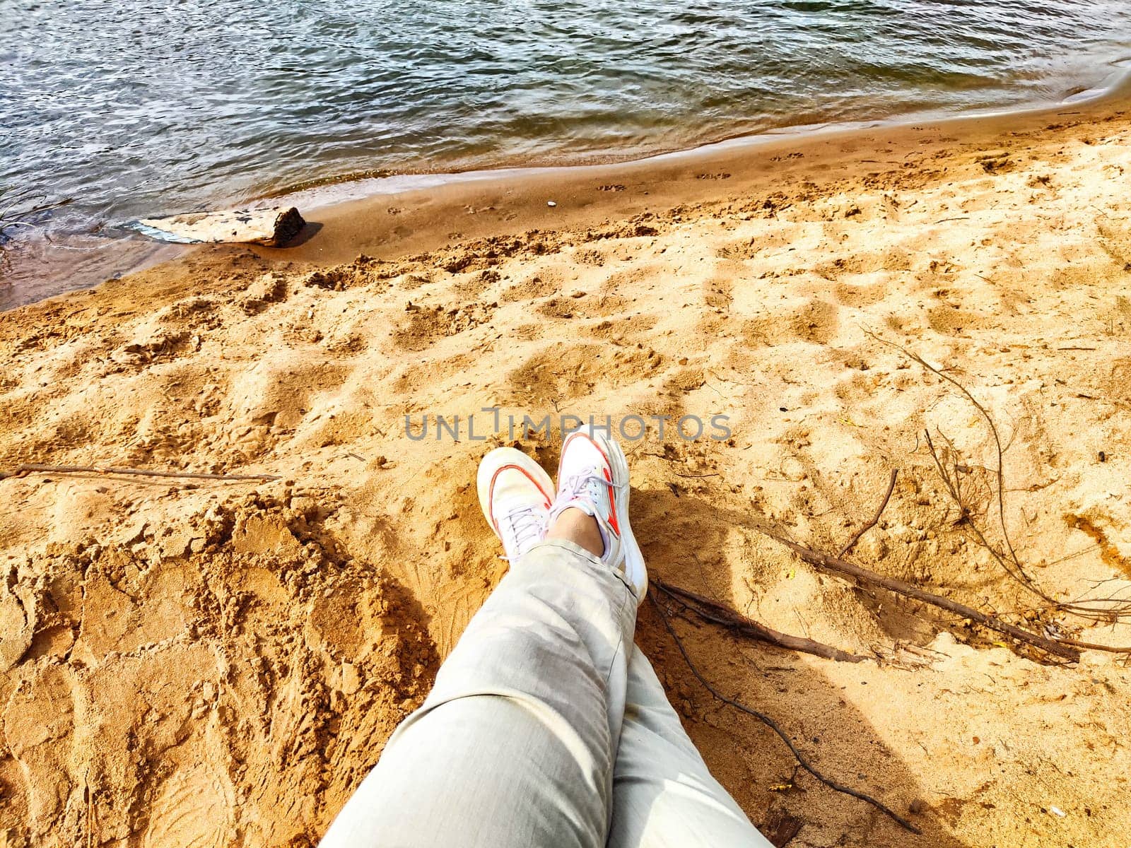 Human feet on sandy beach. The concept of tourism and recreation. Rested legs stretched towards the calm sea