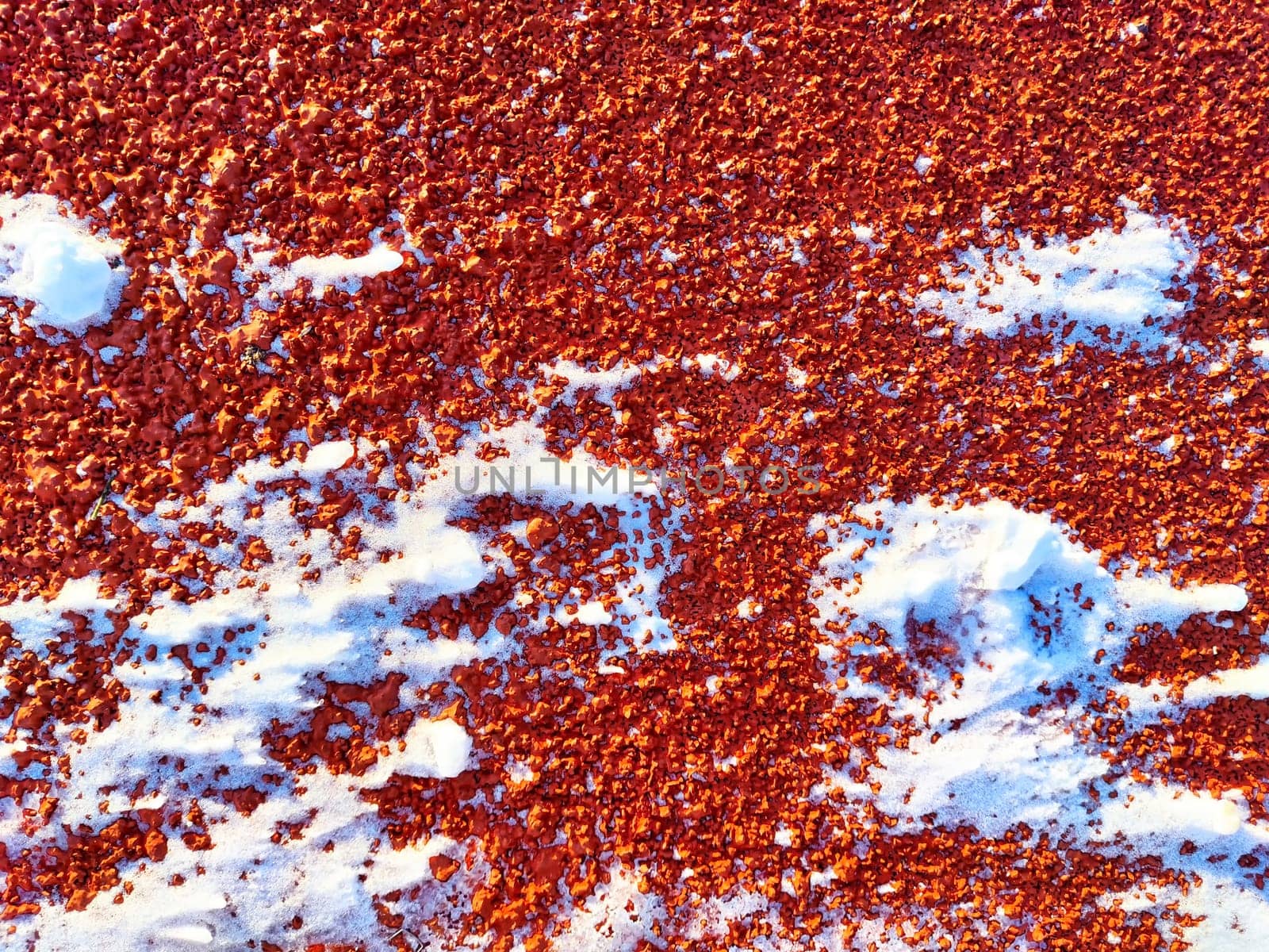 Red pebbles or rubberized textured material and white snow on it. Background, texture, frame, copy space. Contrast of red pebbles and white snow creating a textured backdrop by keleny