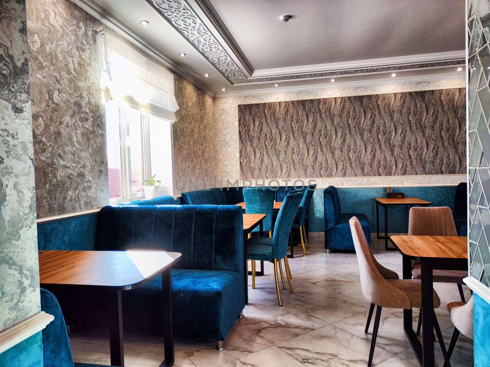 Elegant Restaurant Interior With Plush Seating and Natural Light. A cozy and stylish dining area with blue velvet chairs by keleny