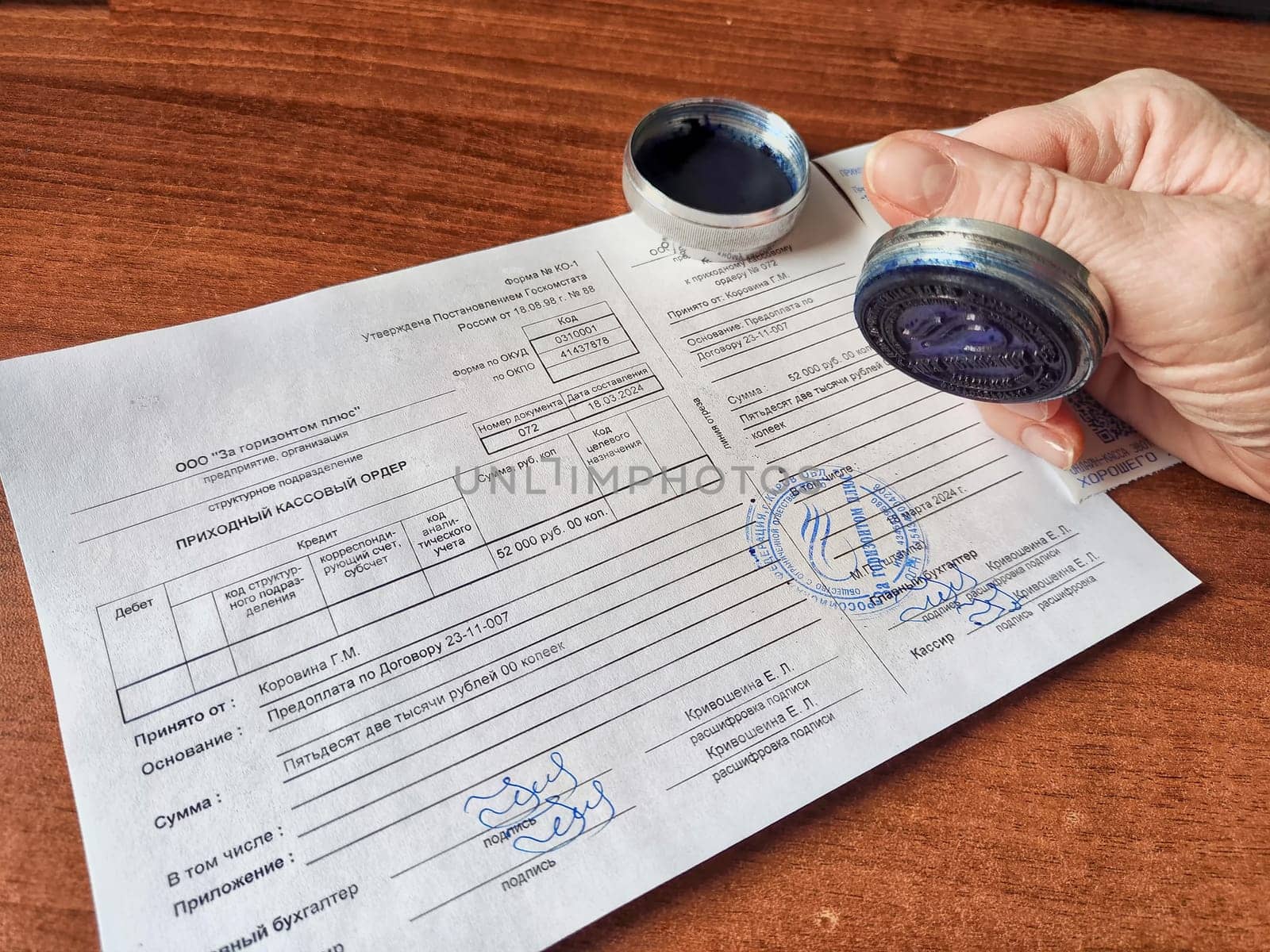 Kirov, Russia - March 18, 2024: Close-up of hand pressing a seal onto paper. Woman Applying Seal to Official Document on Table