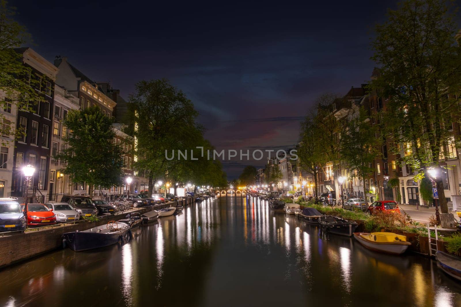 Netherlands. Summer night on the embankment of Amsterdam. Parked cars and lamps on embankments. Boats moored along the banks of the canal