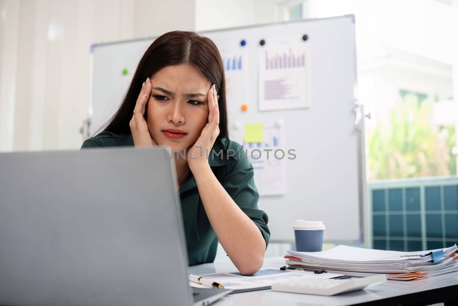 Stressed overwhelmed businesswoman working with computer laptop while having headache in the office.