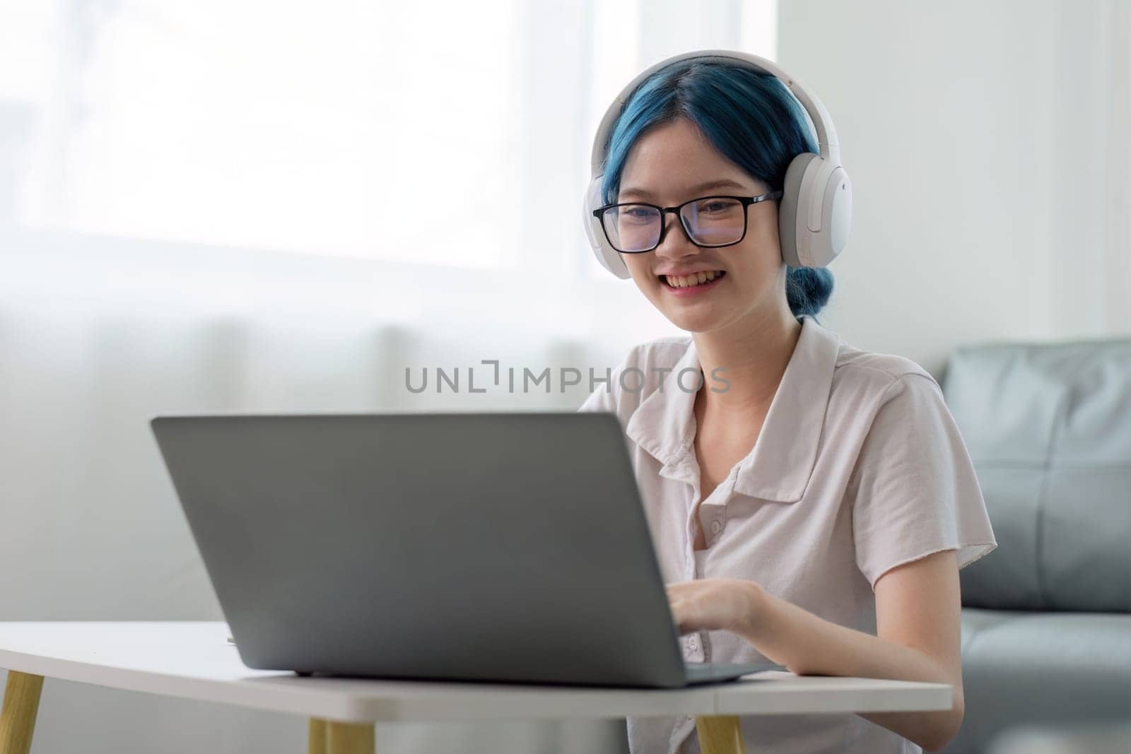 Smiling girl student wear headphone study online with teacher, happy young asian woman learn lecture watch webinar write notes look at laptop sit in home, distant education by nateemee