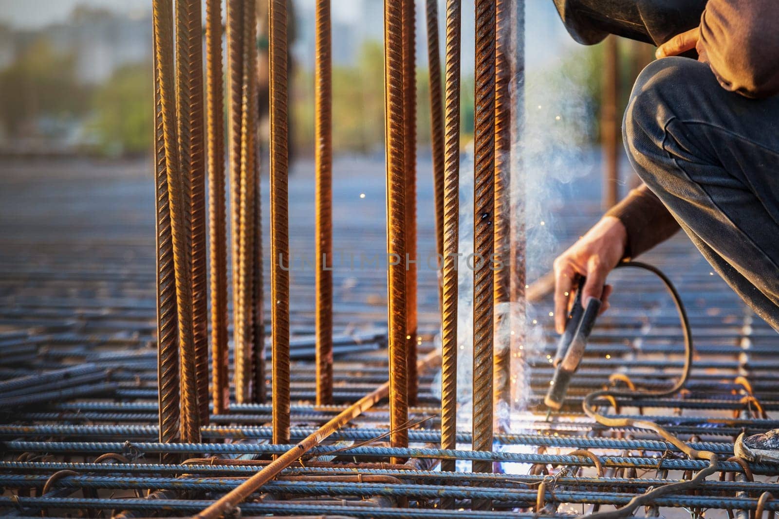 A welder welds a steel frame from reinforcement for reinforced concrete structures at a construction site by Rom4ek