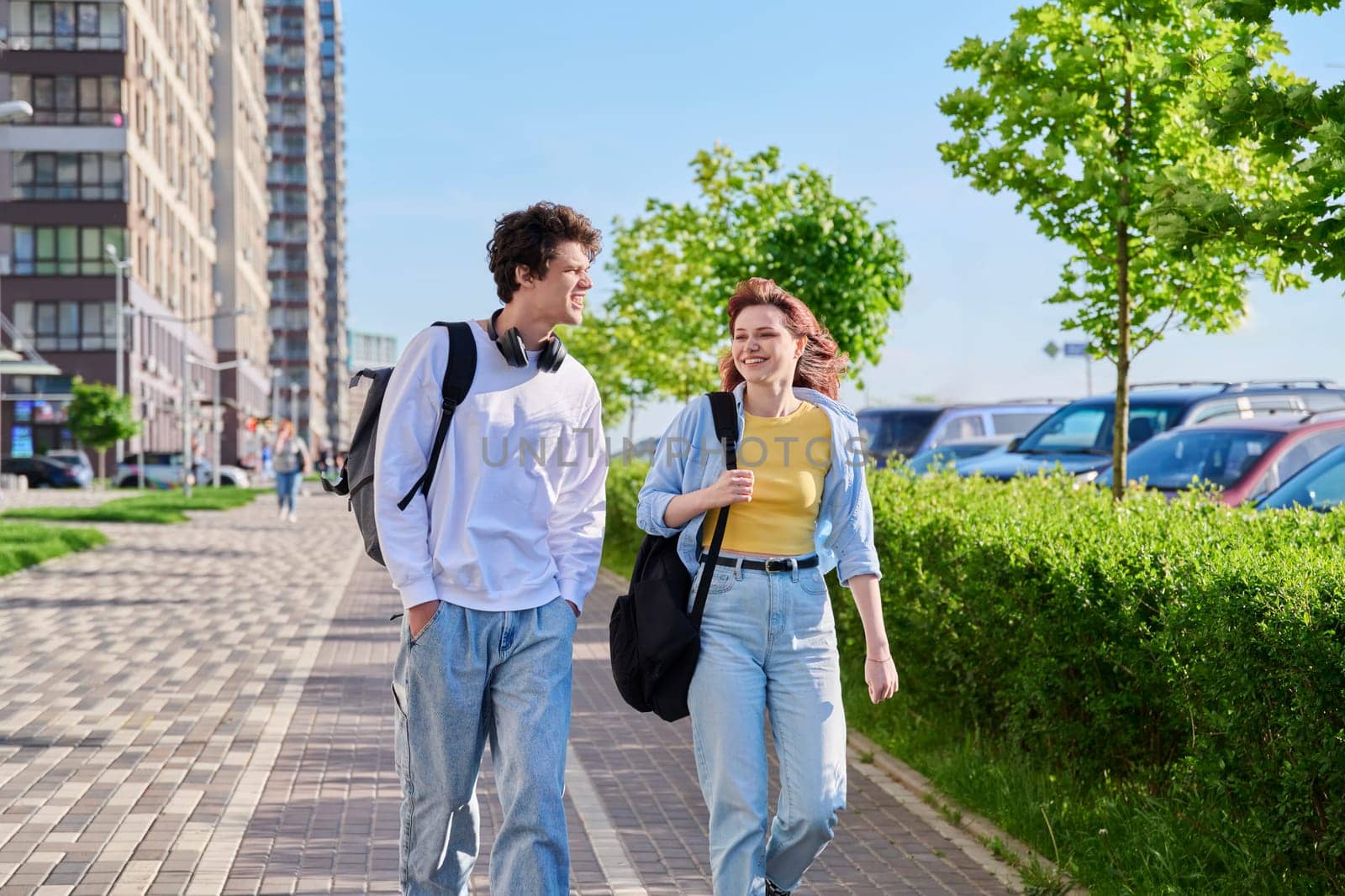 Talking walking friends, guy and girl, university college students walking together along street of modern city. Youth 19-20 years old, friendship, communication, urban lifestyle concept