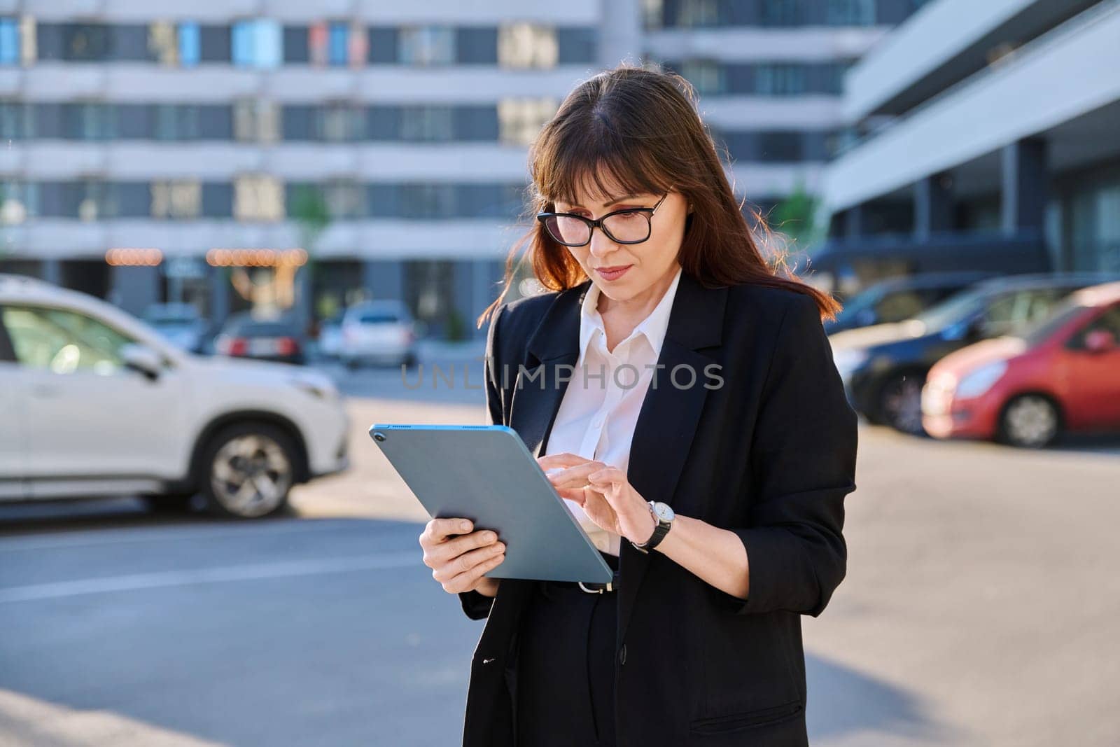 Mature woman manager professional agent entrepreneur using digital tablet for work, modern city. Female leader businesswoman in business suit, outdoor, internet software applications apps technology