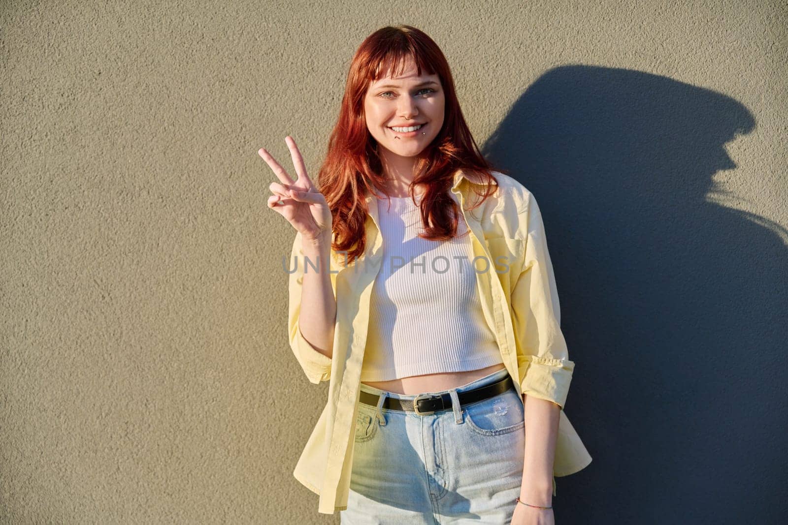 Young smiling beautiful attractive red-haired hipster female with facial piercing looking at camera outdoor, gray solar wall background. Beauty, fashion, piercing, style, lifestyle youth concept