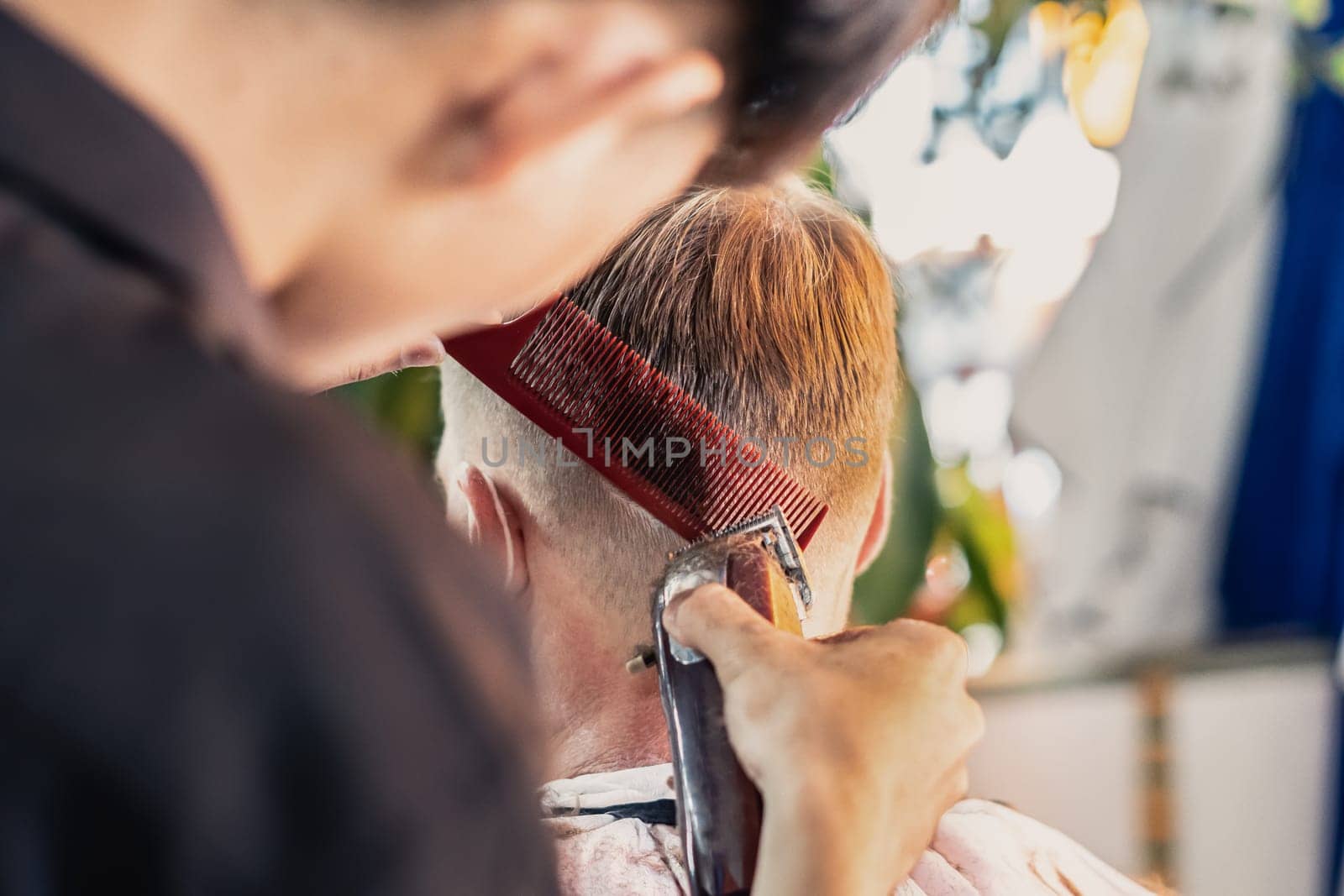 Neat young Vietnamese hairdresser makes haircut to male. Back view. Professional skills.