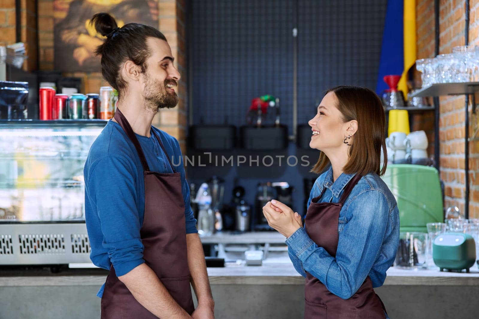 Small business team, successful colleagues partners workers young man and woman in aprons talking at workplace in restaurant coffee shop cafeteria. Cooperation, partnership, teamwork, staff, work