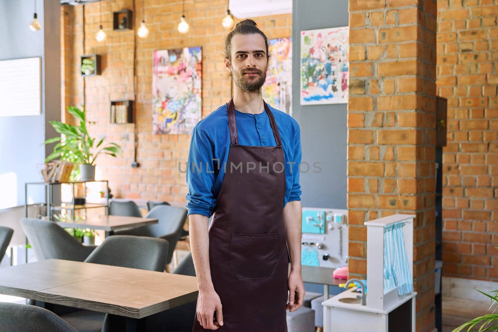 Confident successful young man service worker owner in apron, handsome male looking at camera in restaurant cafeteria coffee pastry shop interior. Small business staff occupation entrepreneur work