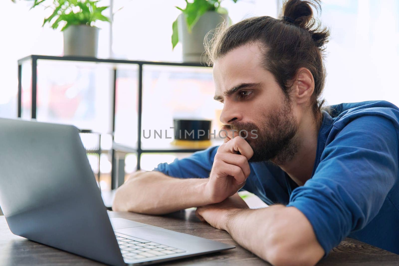 Serious tired young man looking at laptop screen by VH-studio