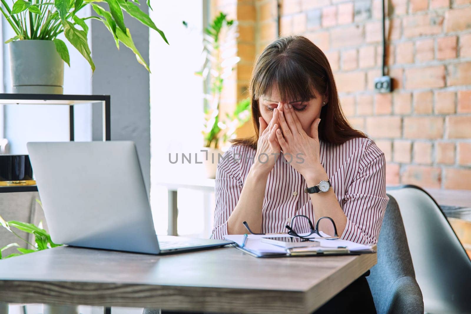 Mature tired worried tense woman at workplace experiencing stress headache by VH-studio