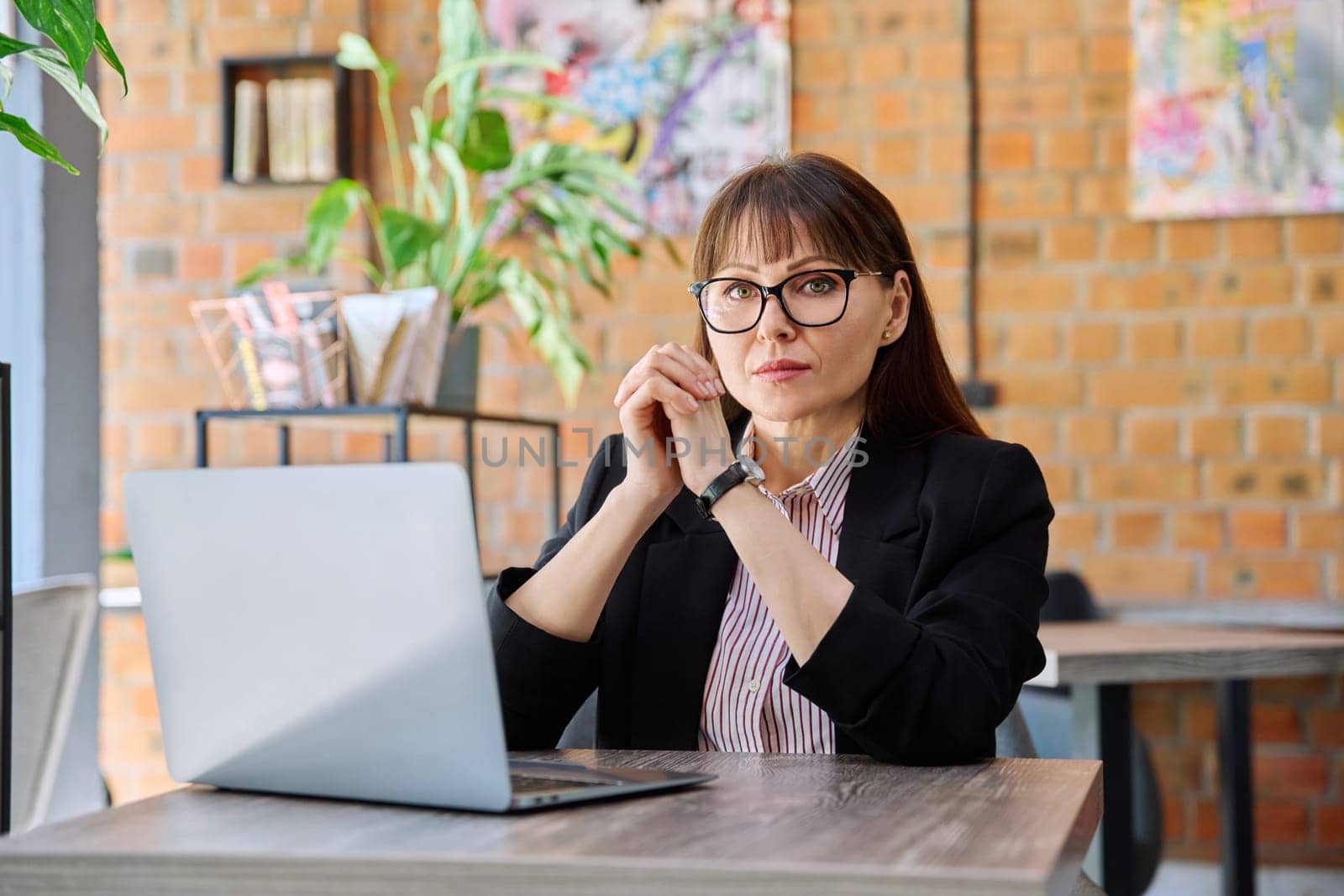 Middle-aged business confident woman working remotely at table with laptop computer looking at camera in coworking cafe. Business, mature people, success, leadership, management, empowerment concept