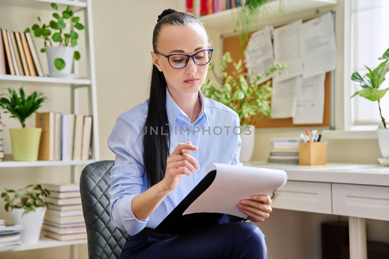 Portrait of female psychologist with clipboard at workplace in office by VH-studio