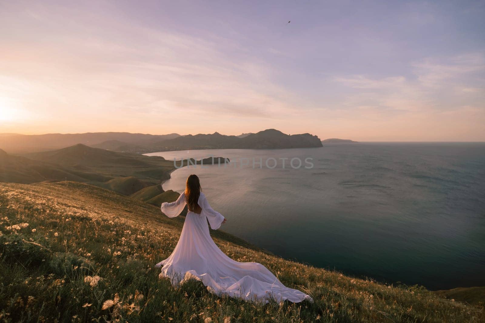A woman in a white dress stands on a hill overlooking a body of water. The scene is serene and peaceful, with the woman's dress billowing in the wind. The combination of the woman's elegant attire. by Matiunina