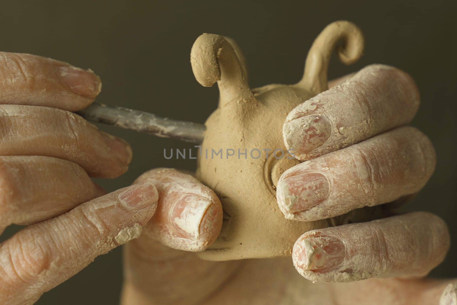 A woman makes holes using a tool in a clay craft - a candlestick. Close-up. Hobbies and creativity.
