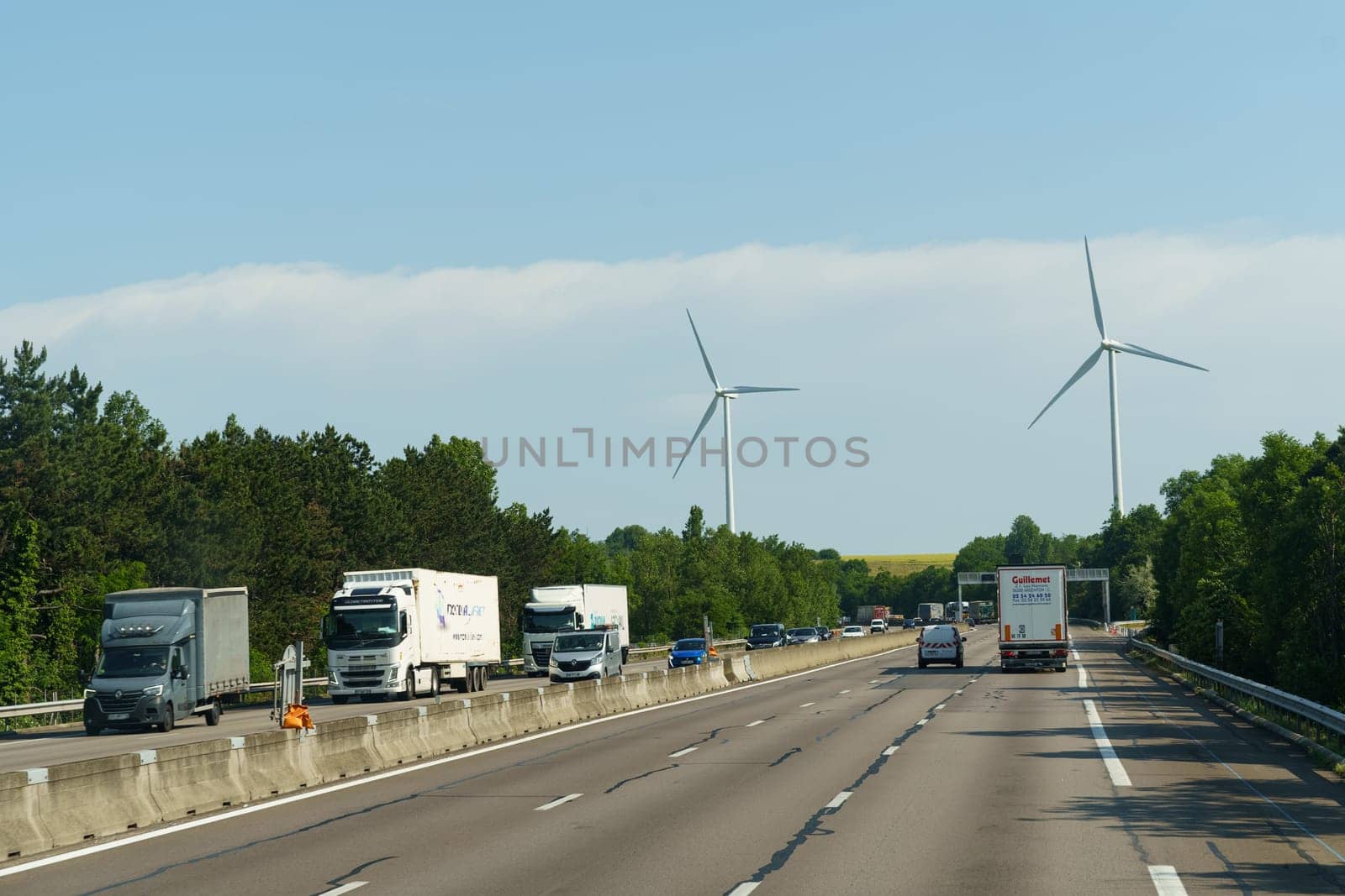 Vaugry Gard, France - May 30, 2023: A highway filled with heavy traffic running parallel to a line of towering wind turbines generating renewable energy.