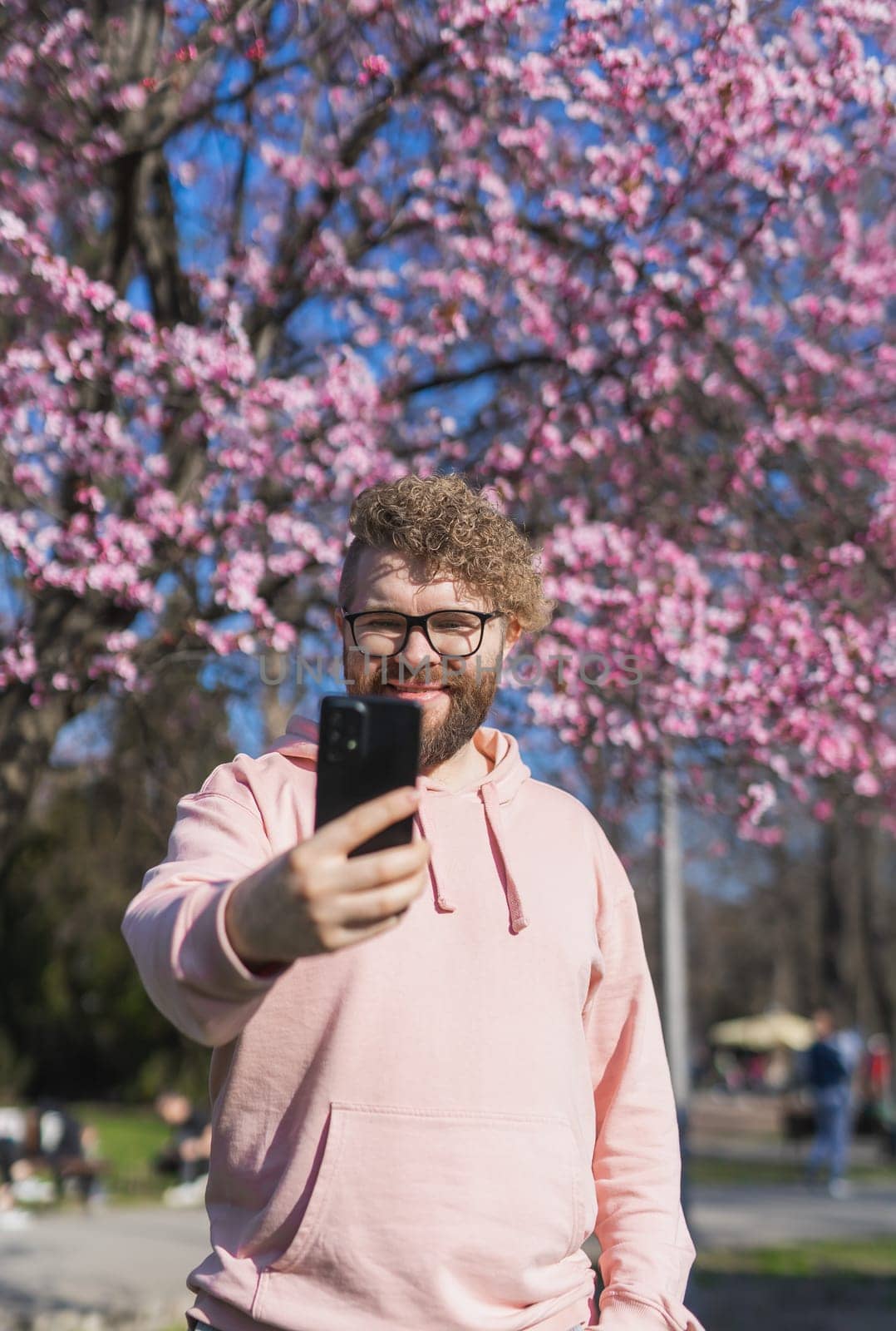 Spring day. Bearded man in pink shirt talking by phone. Spring pink sakura blossom. Handsome young man with smartphone. Fashionable man in trendy glasses. Bearded stylish man. Copy space by Satura86