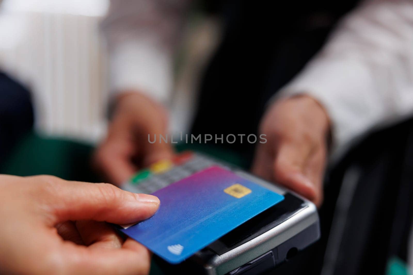 Detailed view showing hands of hotel employee holding pos terminal towards tourist paying with debit card. Close-up of cashless payment using credit card machine at lounge area of ski resort.