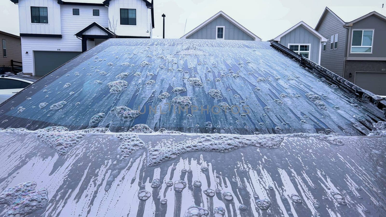 A Tesla Cybertruck undergoes a thorough wash, its unique and angular exterior covered in soap suds, highlighting the vehicle sleek design and durable surfaces.