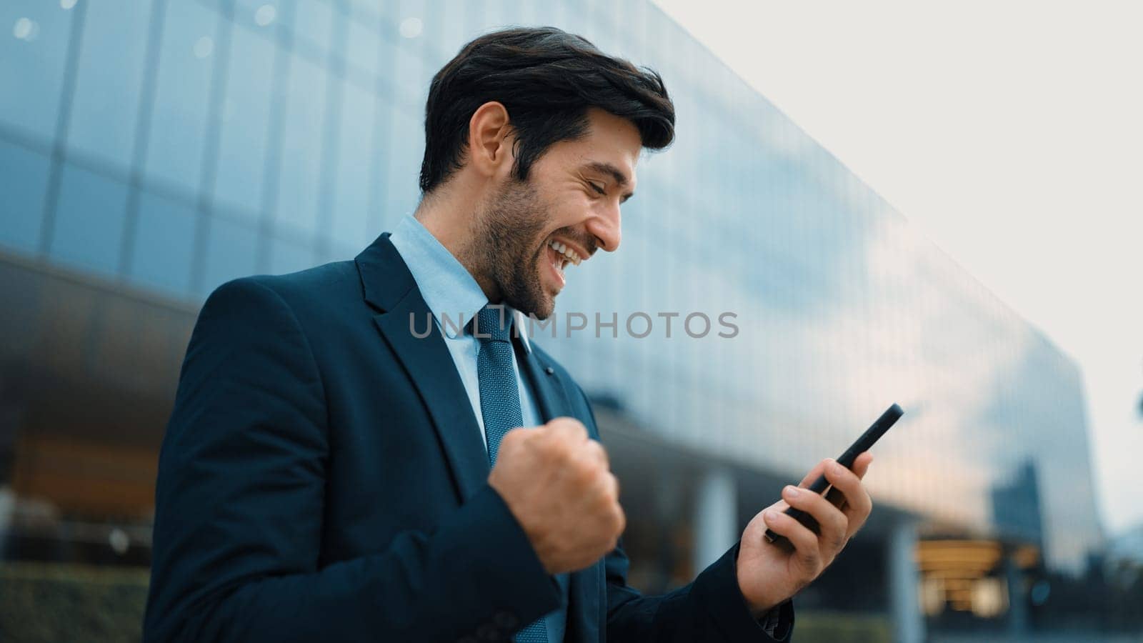 Successful business man celebrate increasing sales while standing. Happy project manager or leader proud with successful project, getting a promotion, getting a job while holding a phone. Exultant.