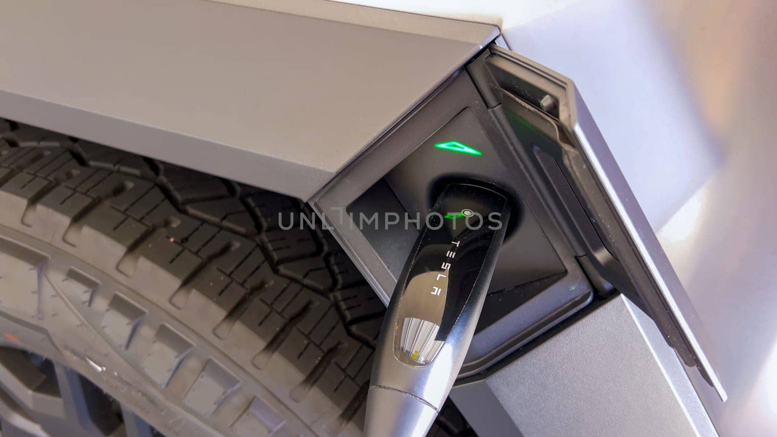 Denver, Colorado, USA-April 28, 2024- This image showcases the charging connector of a Tesla Cybertruck securely plugged into its port, highlighted by the green indicator lights, signifying active charging status in a close-up view.
