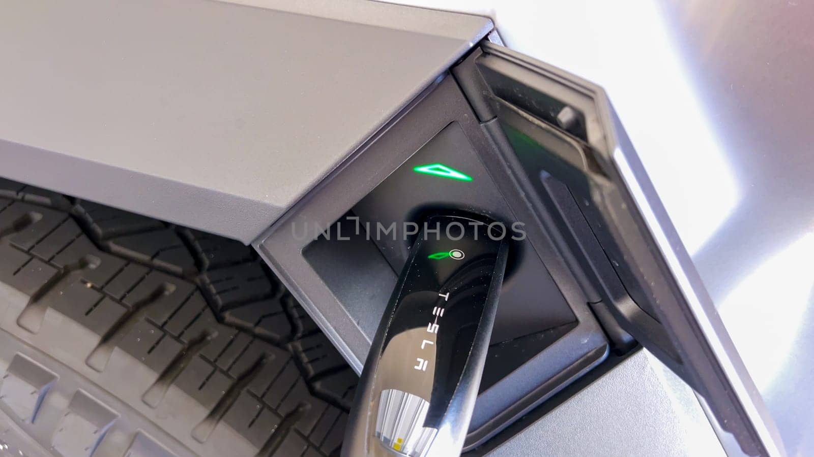 Denver, Colorado, USA-April 28, 2024- This image showcases the charging connector of a Tesla Cybertruck securely plugged into its port, highlighted by the green indicator lights, signifying active charging status in a close-up view.