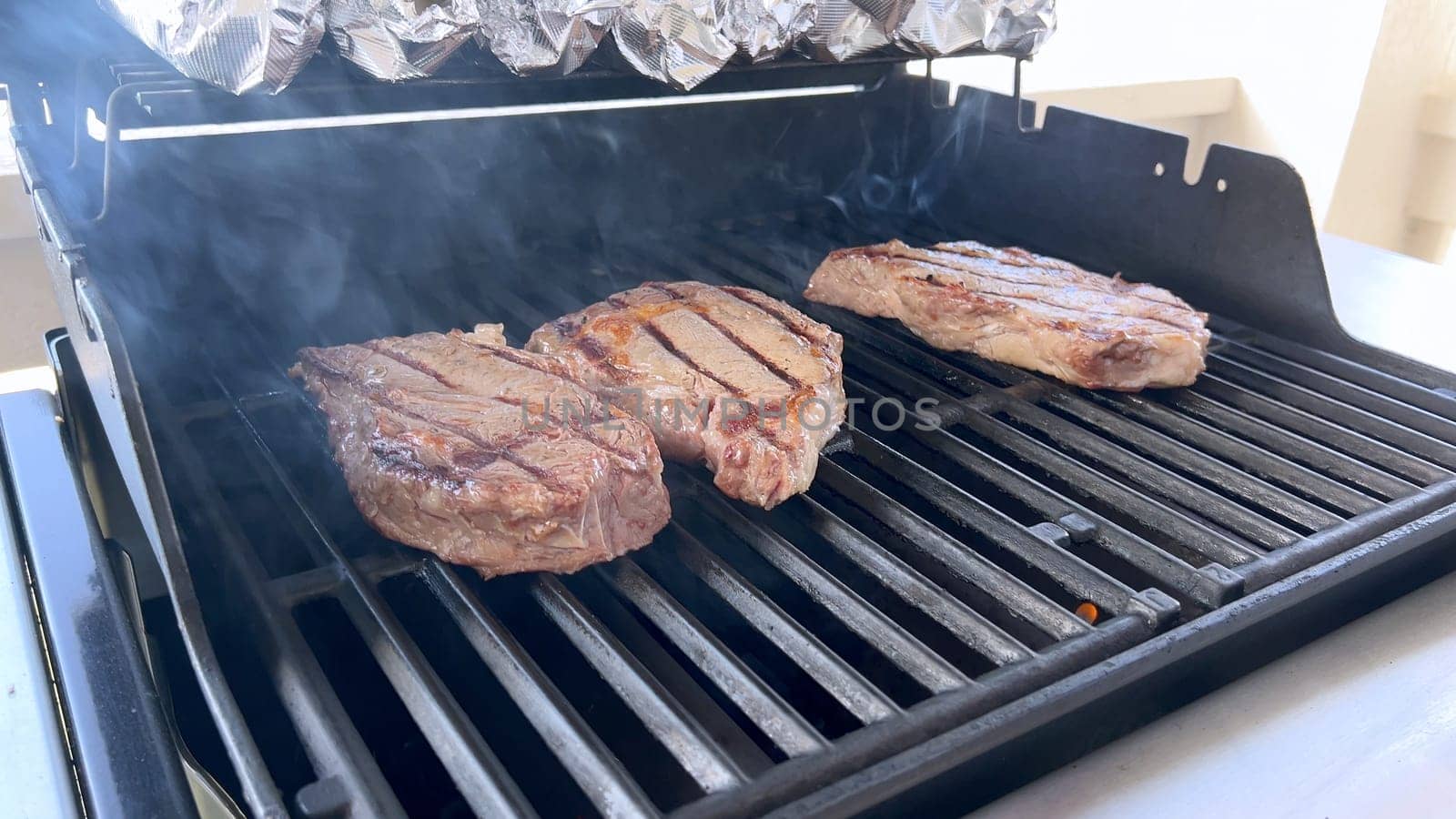 A person uses tongs to flip juicy steaks on a grill, with flames licking the meat, captured in a moment of intense heat and sizzle, showcasing a classic outdoor cooking experience.